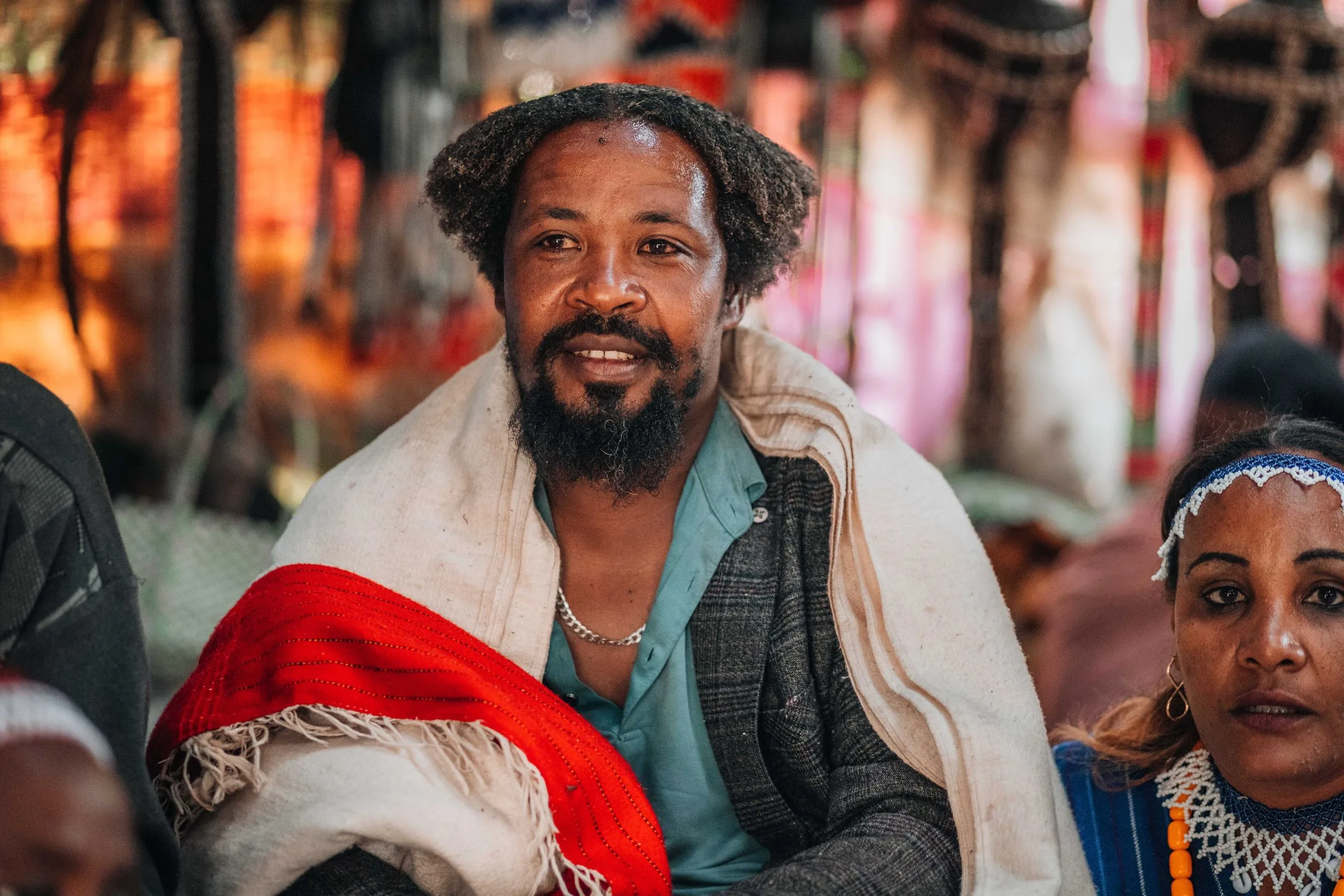 A smiling Ethiopian man with a beard, wearing a white gabi with a red border over a jacket