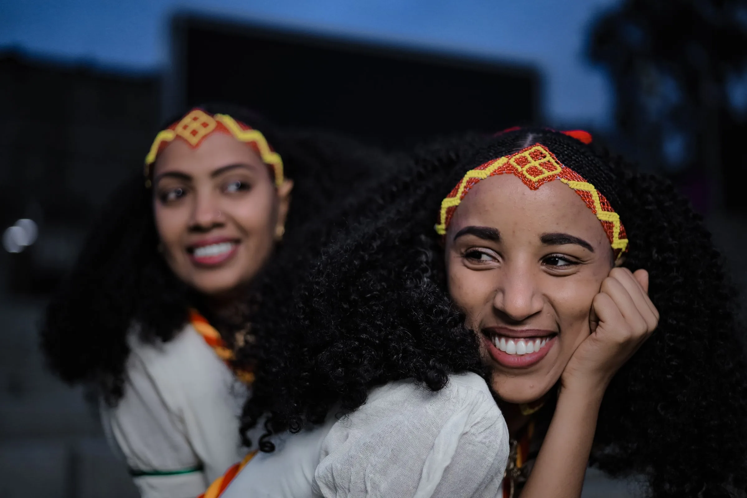 Two smiling Ethiopian women in traditional dress and beaded headbands